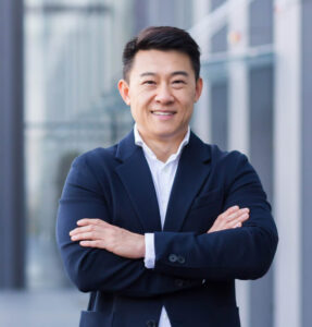 Person in navy suit with crossed arms standing in front of a glass building.